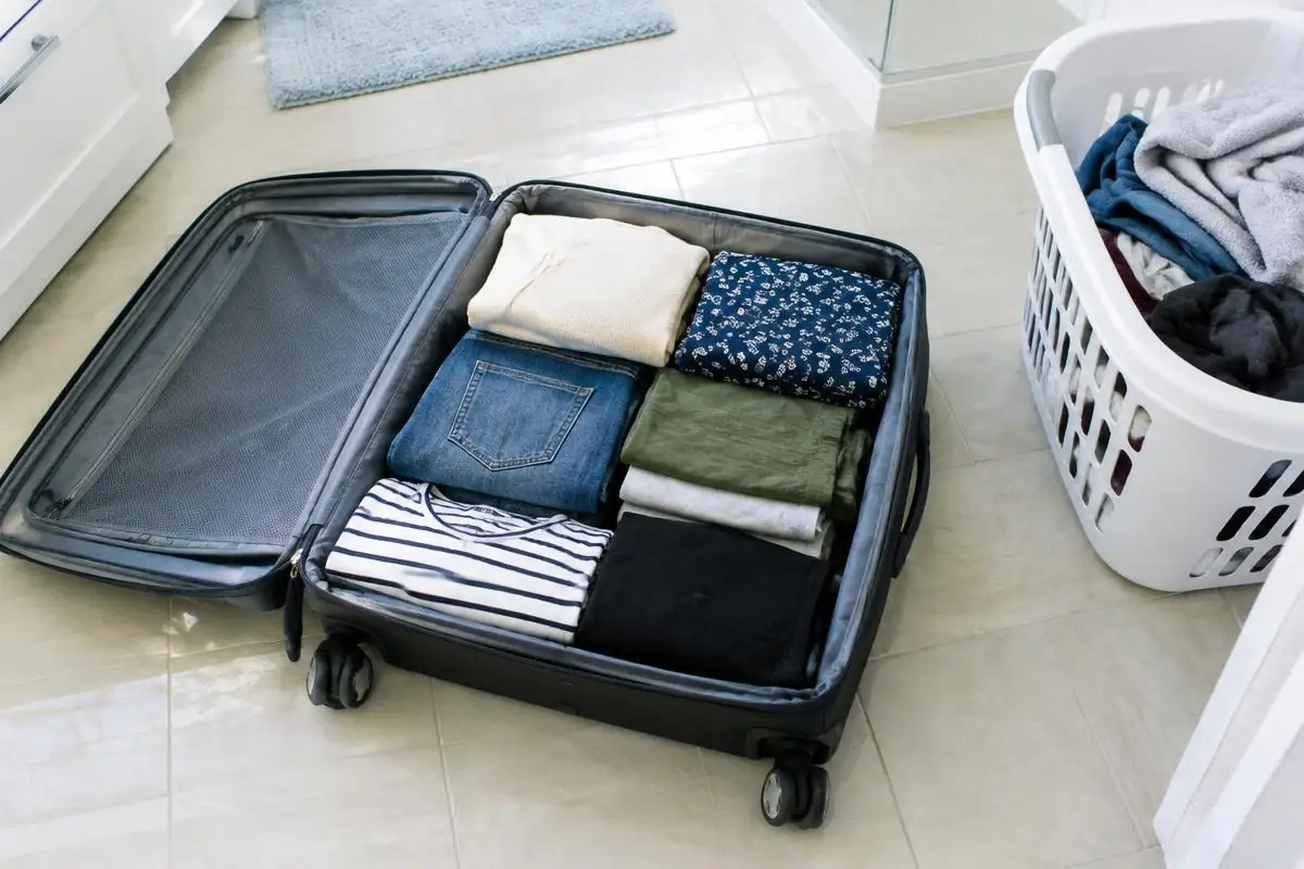 Valise ouverte posée sur un carrelage de salle de bains à côté d’un panier à linge